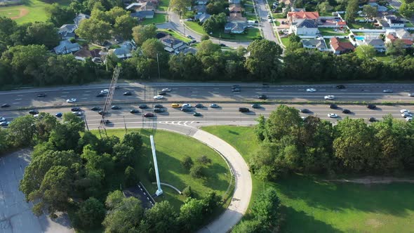 An aerial view of a parkway in the evening at rush hour. The camera truck left over a nearby park wh alt