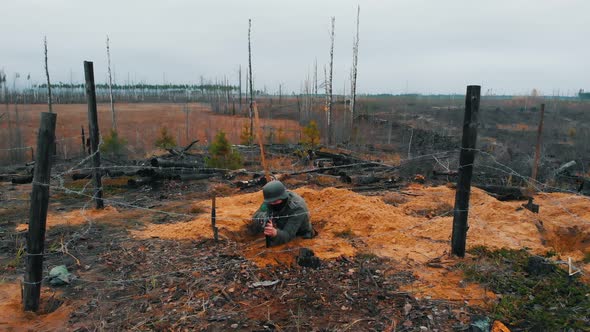 A Soldier Standing in the Trench with a Rifle in Hands - Sitting Behind an Iron Wire and Aiming alt