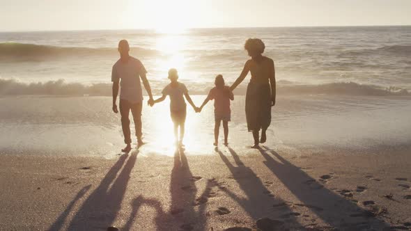 Smiling african american family walking and holding hands on sunny beach alt