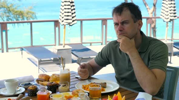 Sad Thoughtful Man Touches Face Touch Chin By Hand Have Breakfast at Restaurant in Hotel Turquoise alt