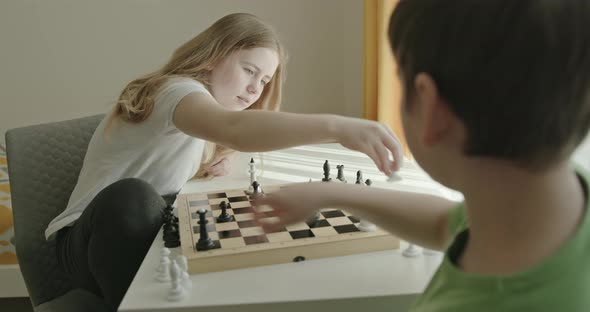Siblings Playing Chess at Home. Preteen Boy and Girl Sitting at Table and Playing Chess Together alt