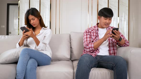 Young Couple sitting on sofa with smartphone ignoring each other alt