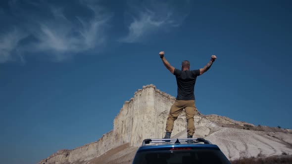 Strong man stands on the roof of his SUV and looks out over a huge canyon