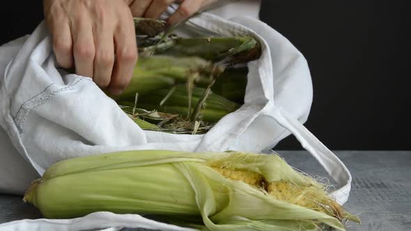 man get fresh ripe ear corn out of white eco fabric cotton tote bag, put on kitchen stone table top