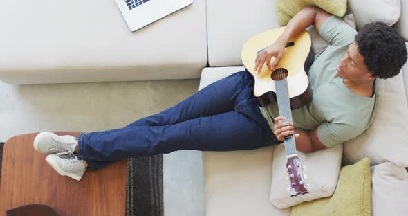 African american man plays guitar and singing, using laptop at home alt