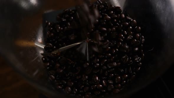 Dark roasted coffee beans falling into grinder machine, top view slow motion