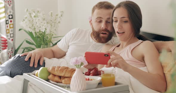 Amazed Man and Woman Watching Video and Smiling in Bed, Young Romantic Couple Talking and Looking at alt