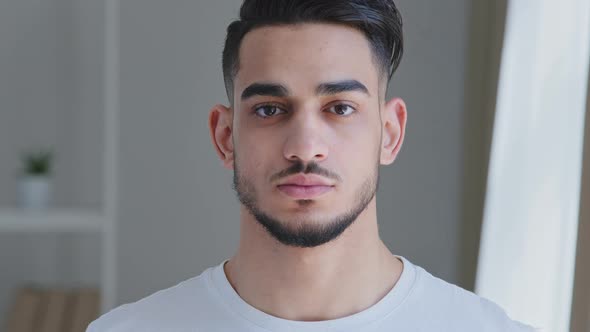 Portrait of Serious Handsome Young Adult Arabic Man with Beard in White Tshirt Stands Posing Indoors alt