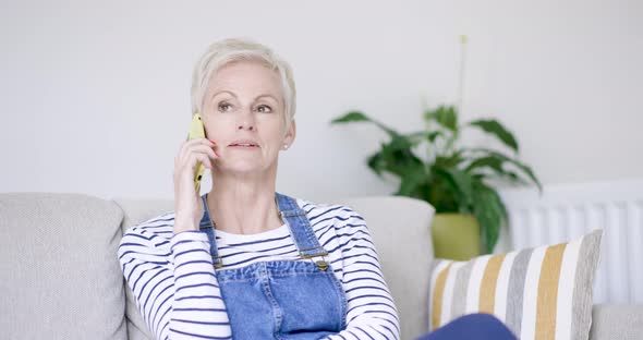 Mature woman sitting on sofa talking on the phone alt