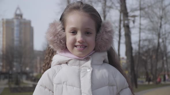 Close-up of Pretty Smiling Girl Posing in Spring Park. Portrait of Cute Little Caucasian Brunette alt