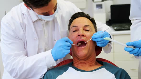 Dentists examining a male patient with tools alt