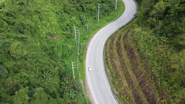 Aerial view of a car running along the mountain road through tropical forest in countryside by drone