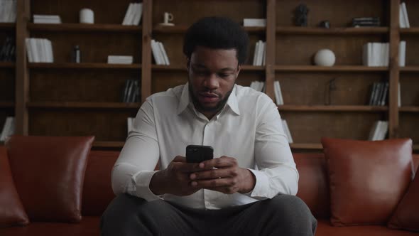 Young Adult Africanamerican Man Browsing on His Smartphone in Loft Apartment alt