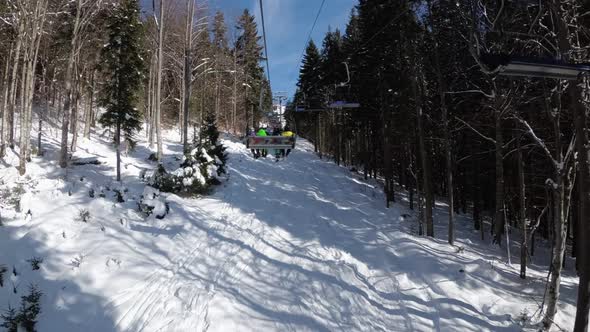 POV From Ski Chair Lift Between Pine Forest and Skiers Rising Up on Cableway alt
