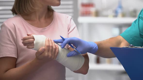 Doctor Consulting Female Patient With Arm Elastic Bandage, Writing Result