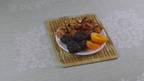 Apricots Prunes Dates Walnuts on a White Saucer Standing on a Bamboo Napkin alt