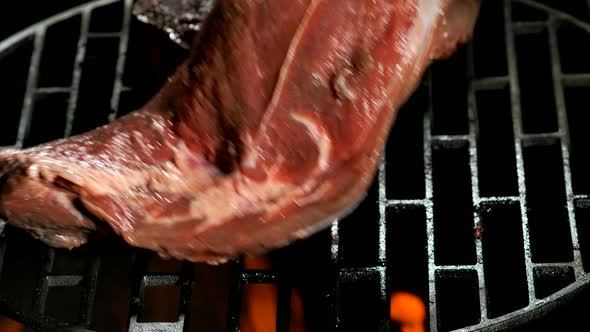 Tongs are Placing a Raw Steak on the Round Grill on the Background of the Fire alt