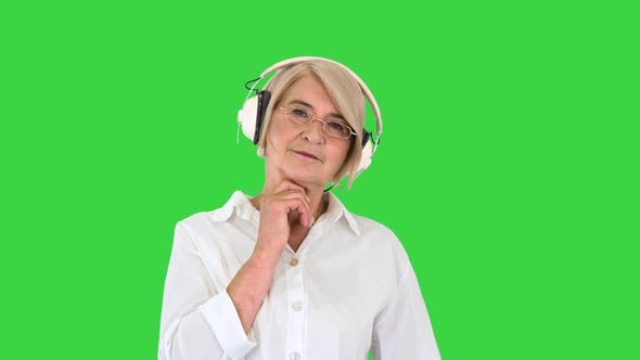Old Intelligent Woman Listening To Music in Headphones on a Green Screen, Chroma Key. alt