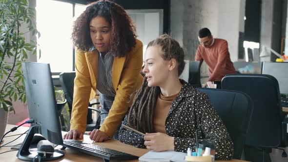 Businesswomen Talking Pointing at Computer Screen Discussing Work in Open Plan Office alt