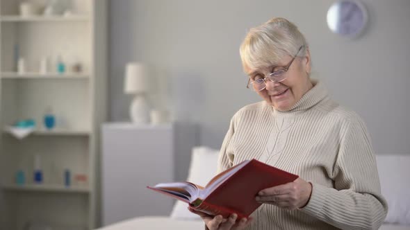 Smiling Aged Woman in Eyeglasses Watching Photo Album alt