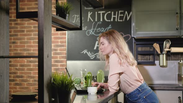 Nice young girl in kitchen and uses laptop to check mail or order goods online. alt