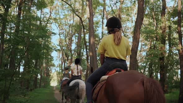 Three young girls on horseback move in a column along the middle of the forest. alt