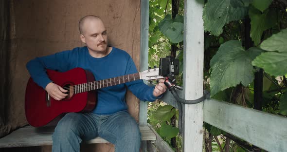 Man with an Guitar is Sitting on Porch Tuning Instrument Using an App on Phone