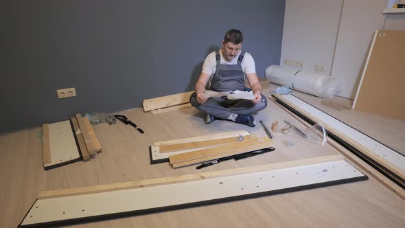 Builder in Overalls Studying Instructions Before Assembling Furniture alt