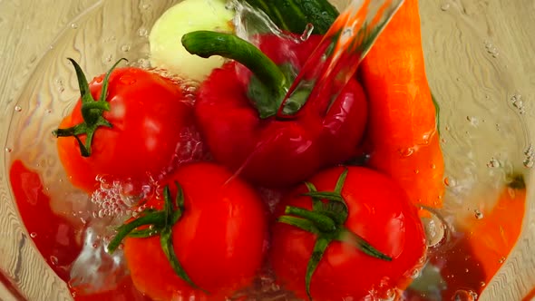 Tomatoes, sweet red peppers, onions, cucumbers and carrots in a glass bowl are washed with water alt