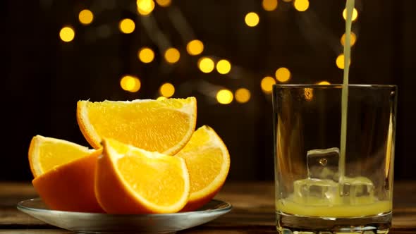 Slices Of Orange On A Plate And Juice Are Poured Into A Glass With Lights In The Background