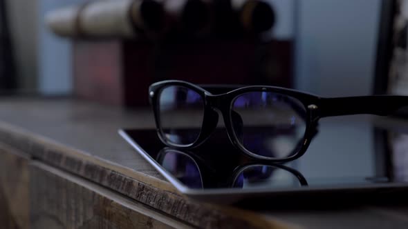 Glasses in Black Rim Lying on a Tablet on a Wooden Dresser in the Room Close Up alt