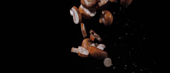 Fresh Chopped Champignons Tossed Up and Fly Around with Water Drops on a Black Background in Slow alt