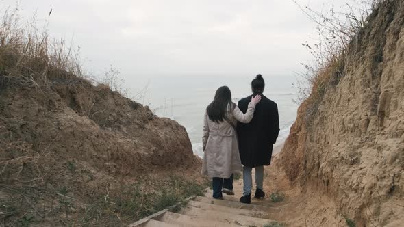 Happy Couple Goes Down the Stairs to the Wild Beach at Sunset alt