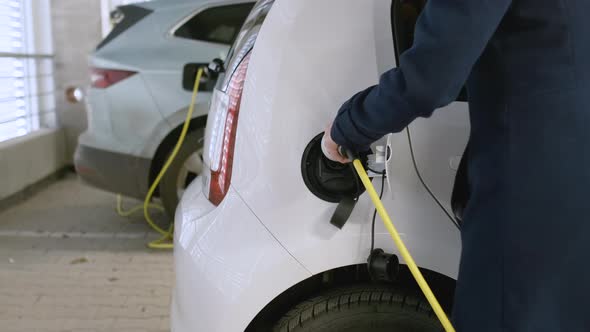 Business Woman Inserting a Charger Into the Electric Car at Charging Point in the Parking on the alt