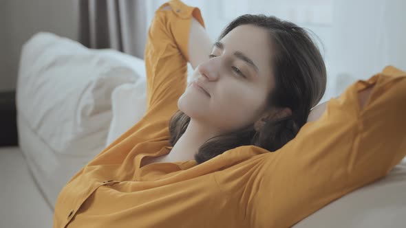 Girl on the Couch Sitting Comfortably with Her Hands Behind Her Head in a Yellow Shirt alt