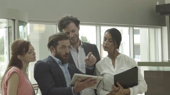 Businessman talking with clients and using digital tablet in lobby alt