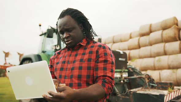 Young African Farmer Using Tablet in Front Og Big Green Tractor Anf Haystack alt