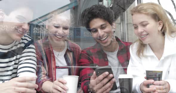 Happy multiracial friends looking at a smartphone in a cafe and laughing. Gro alt