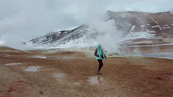 Woman walking on geothermal field with fumaroles and geysers. Area with natural steam vents and mud alt