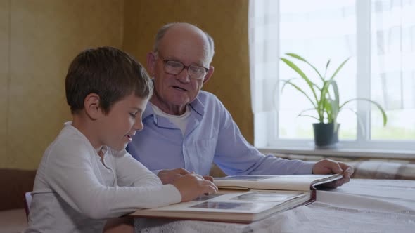 Household Memories, Small Attractive Boy with His Elderly Granddad Have Fun Looking at an Photo alt