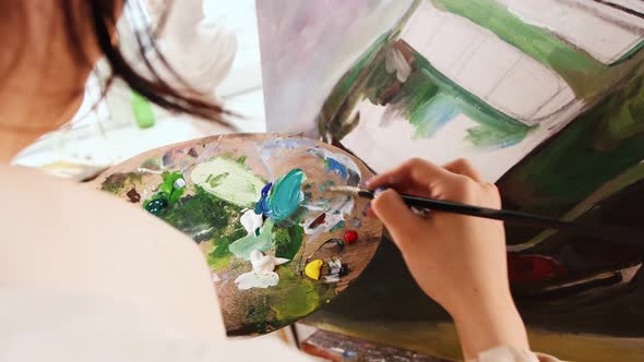 Art Studio  Young Woman in White Shirt Mixing Colors and Drawing a Painting alt