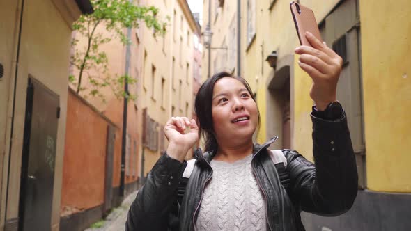 Happy Asian woman having video call on smartphone on small street in Sweden alt