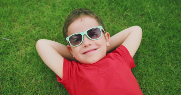Happy Cute Child Lies on the Green Grass a Little Boy in Sunglasses Lies on the Grass Resting alt