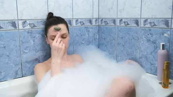 Young Woman is Relaxing Lying in Bath and Doing Face Massage Using Jade Roller