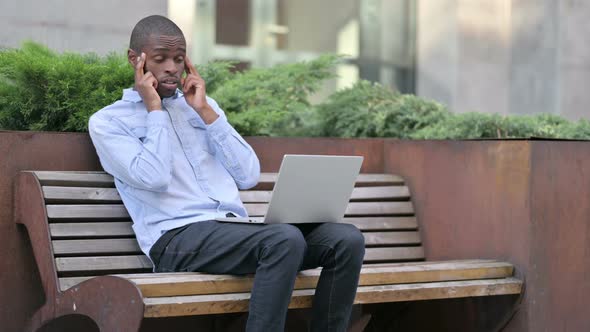 Young African Man with Laptop Having Headache Outdoor  alt