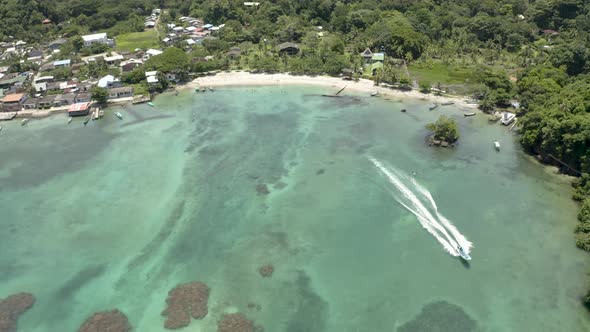 Aerial tilts down to a boat driving along the beach coast. San Blas, Colombia. alt
