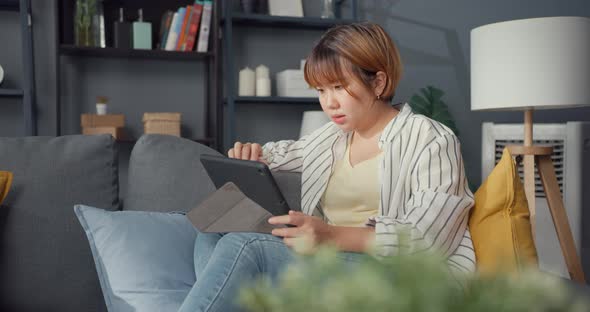 Freelance Asia using tablet online learning in living room at house.