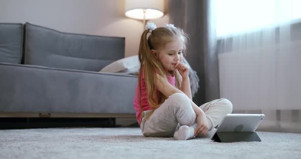 Curious Cute Preschool Kid Girl Using Digital Tablet Technology Device Lying on Carpet Floor Alone
