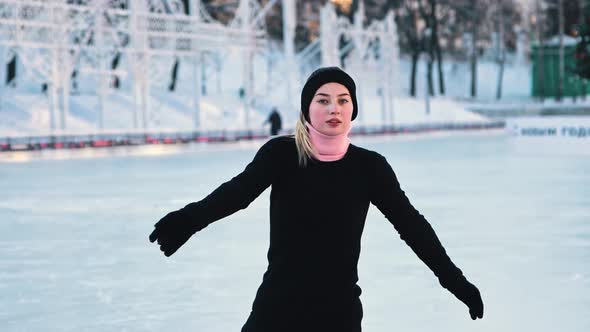 Young Beautiful Woman Training Her Figure Skating on Public Ice Rink and Looking in the Camera alt