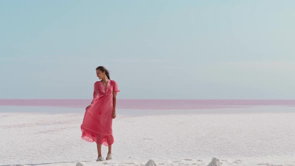 Happy Carefree Elegant Woman in Blowing Pink Dress Enjoys Her Vacation While Walking Along White alt